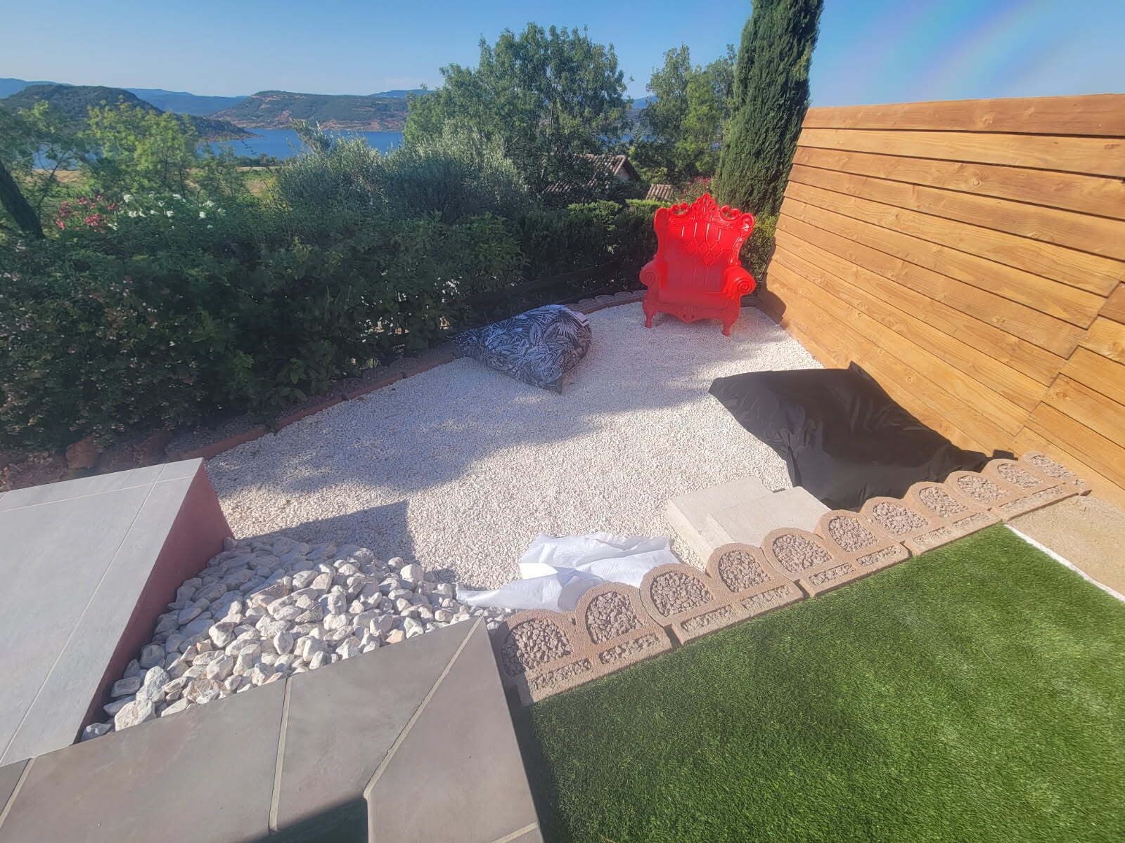 Un jardin avec une terrasse en bois, une chaise rouge et une vue sur la mer.