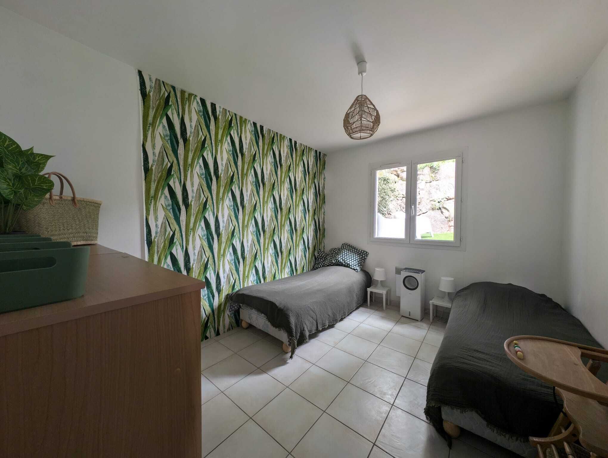 A bedroom with a bed, a small table, a chair, a window, and a wall with a leaf pattern.