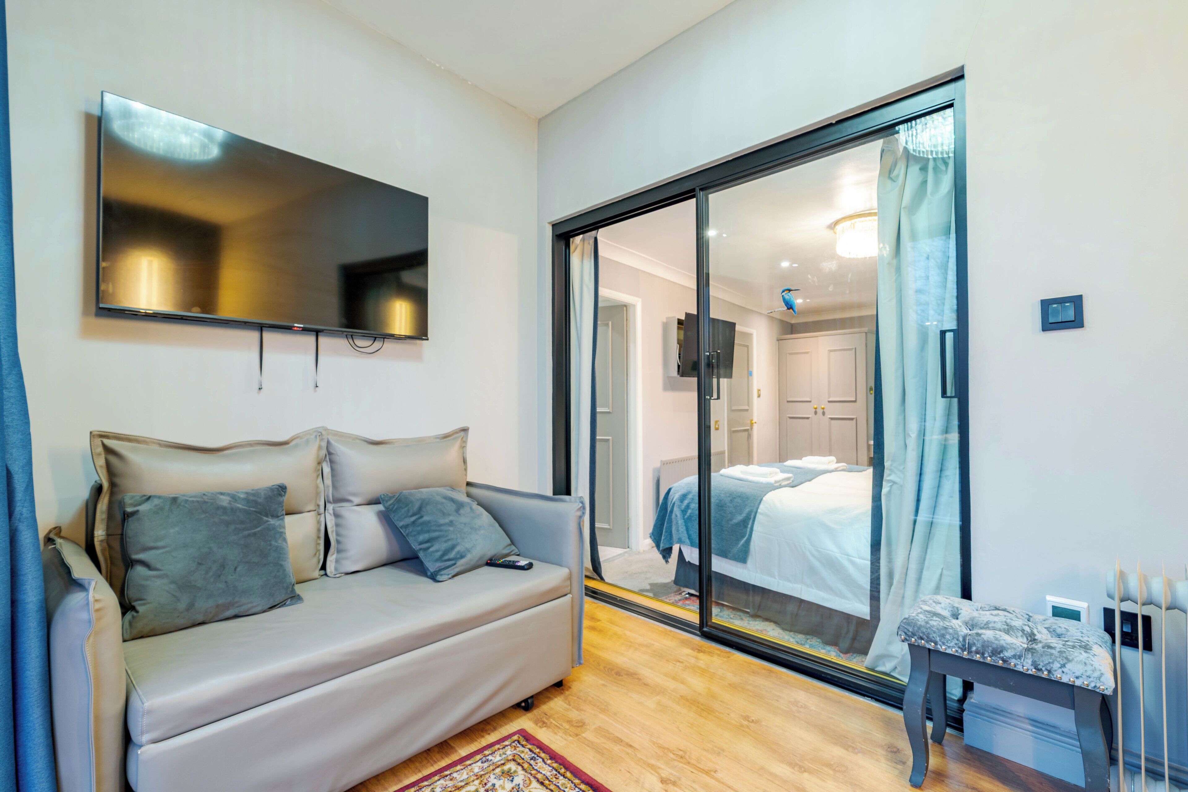 Una habitación moderna con sofá, televisión instalada en la pared y puerta corredera de vidrio que da a un dormitorio.