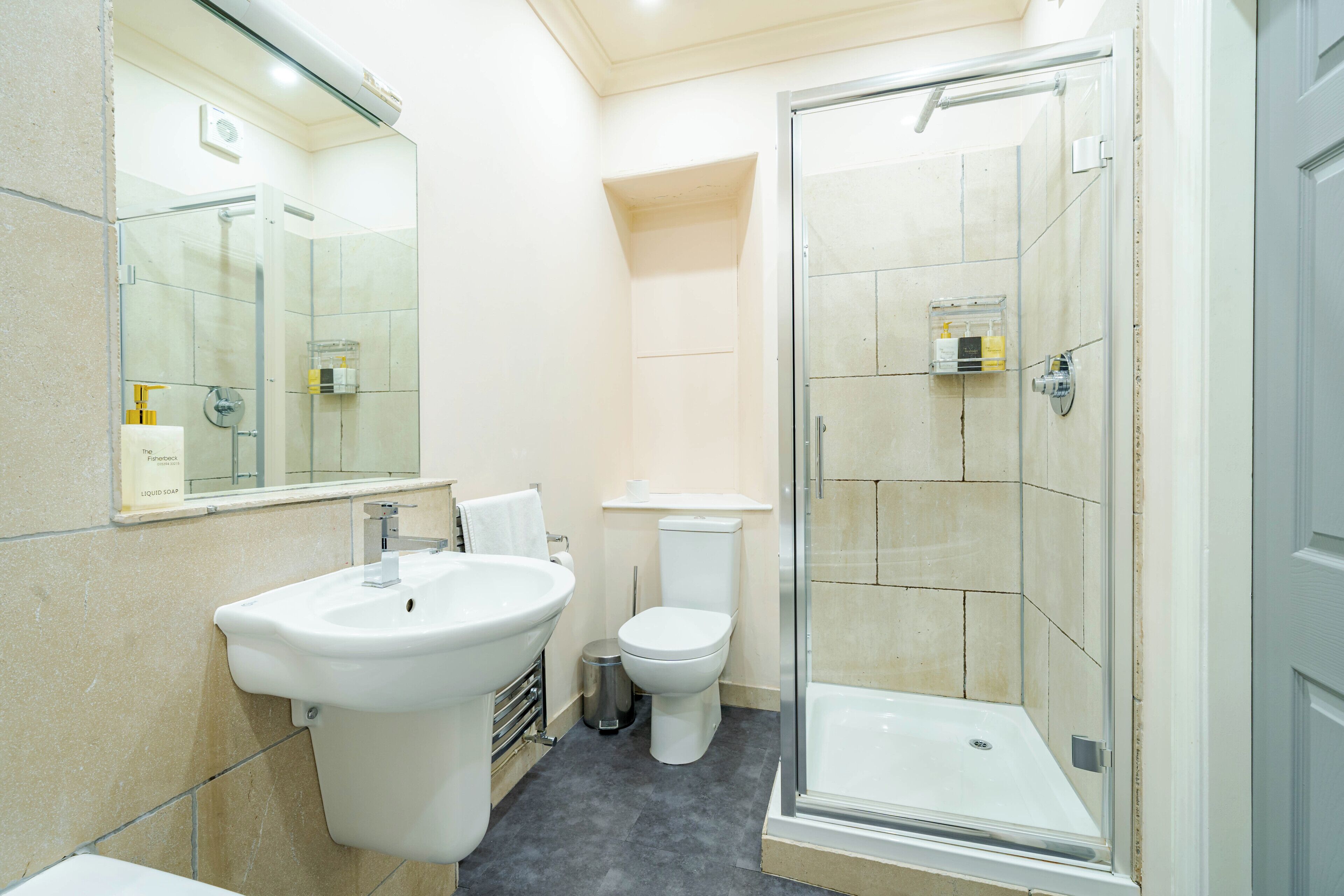 Een moderne badkamer met een glazen douchecabine, een wastafel op een voetstuk en een toilet.