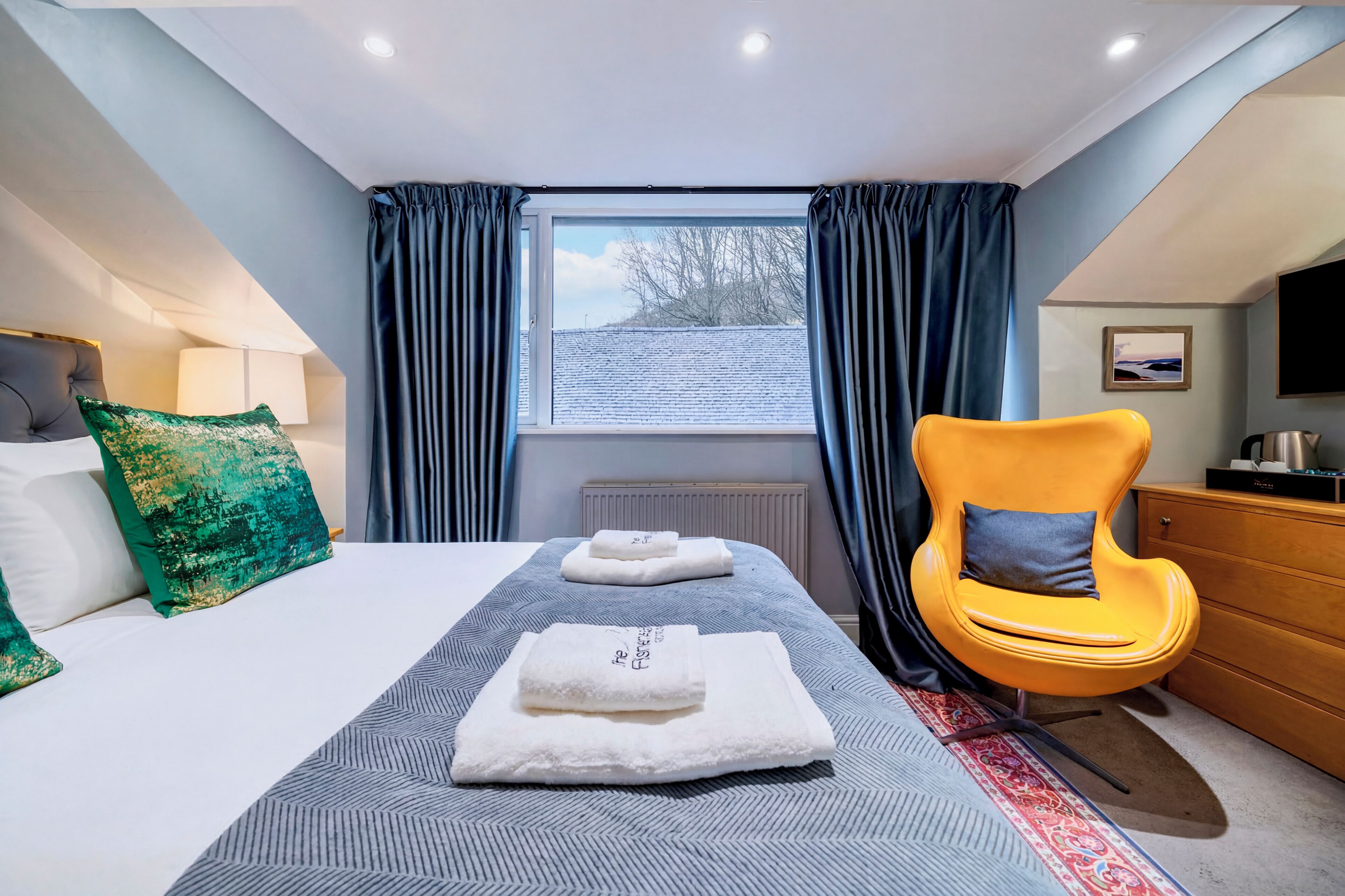 Una habitación de hotel con cama, una silla, ventana con cortinas, radiador y televisor.