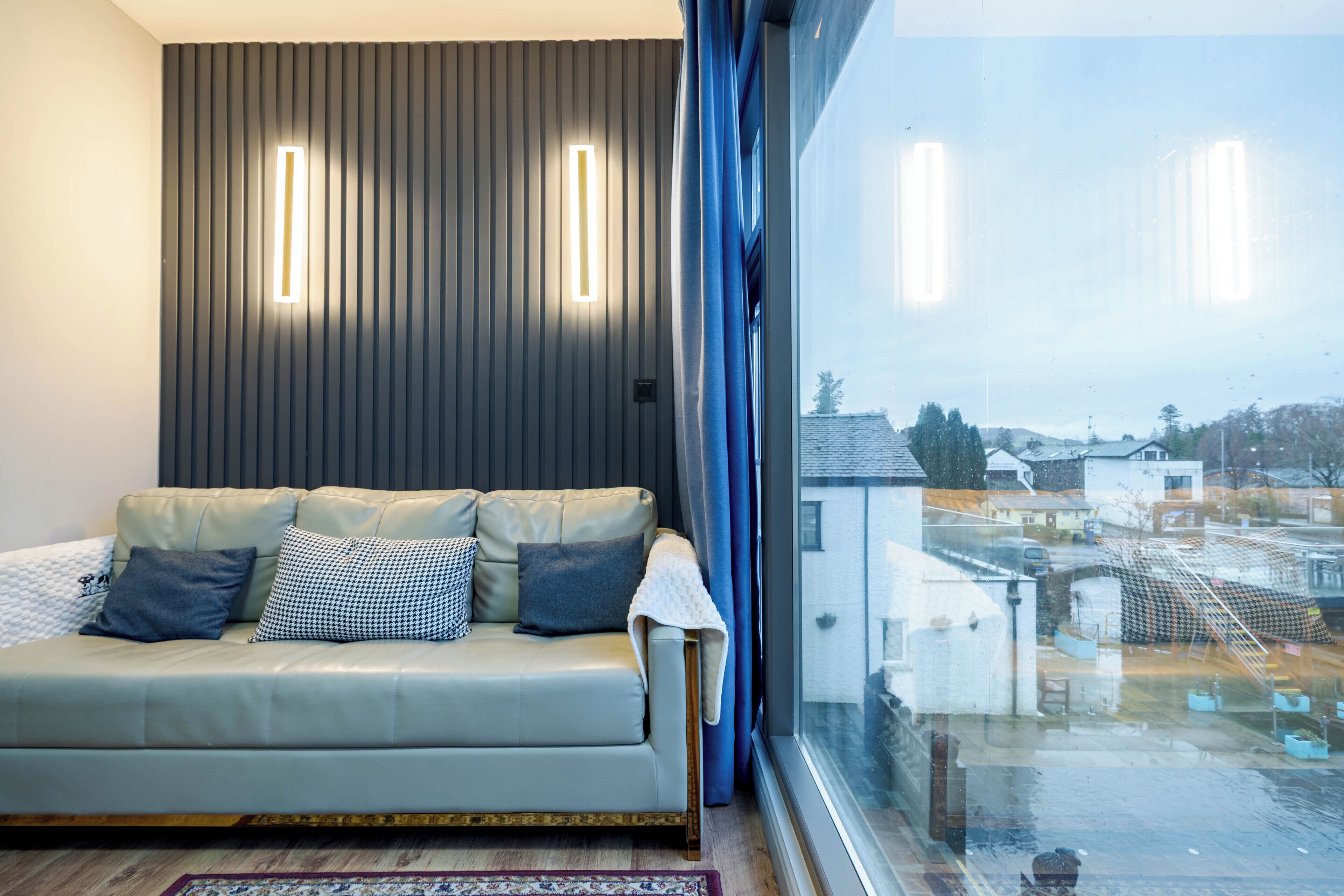 A modern living room with a sofa, pillows, and a view through a large window.