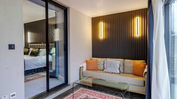 Un salon moderne doté d’une cloison en verre, d’un canapé avec des coussins, d’un tapis à motifs et d’un luminaire fixé au mur.