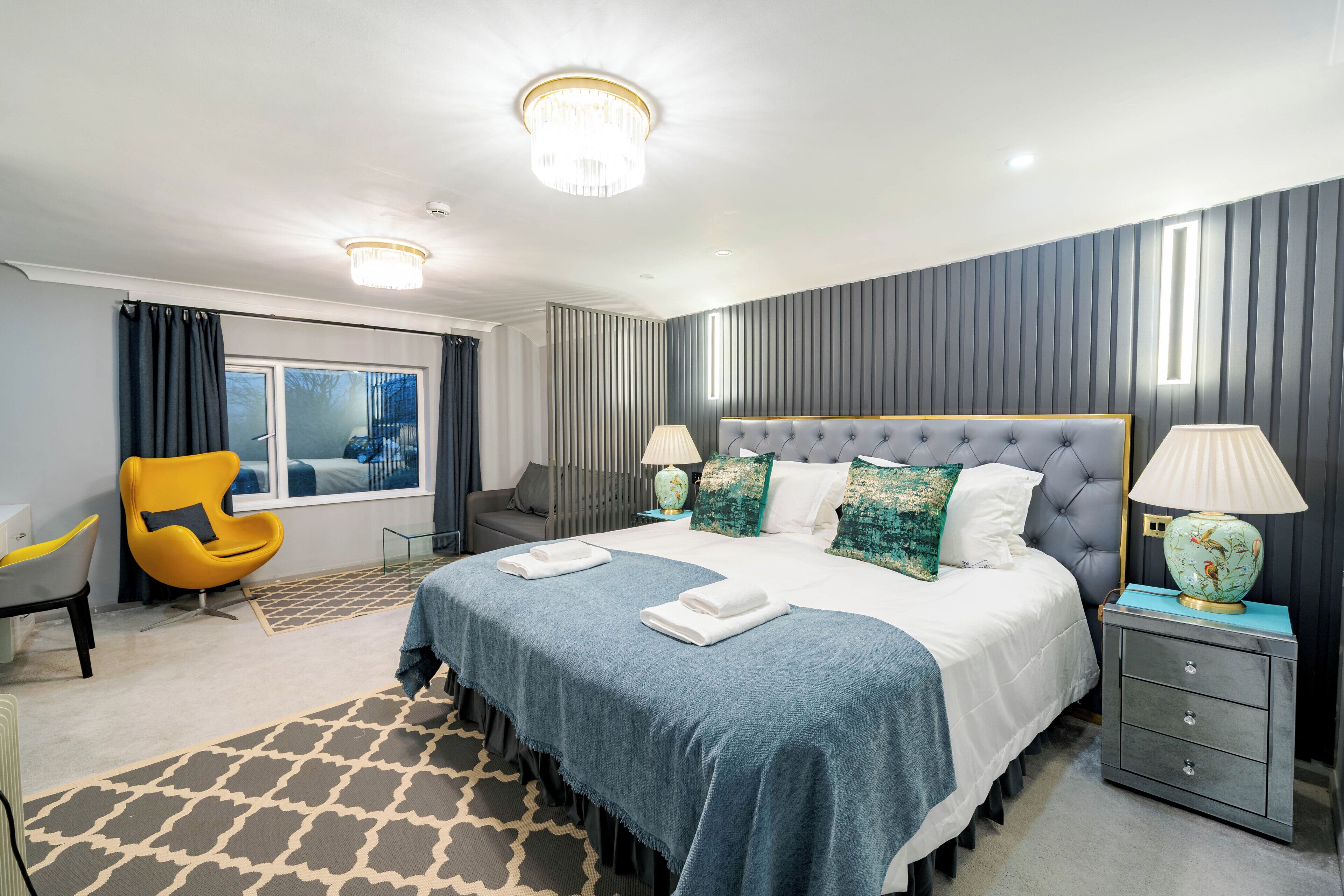 A hotel room with a large bed, a chair, a nightstand, and a window.