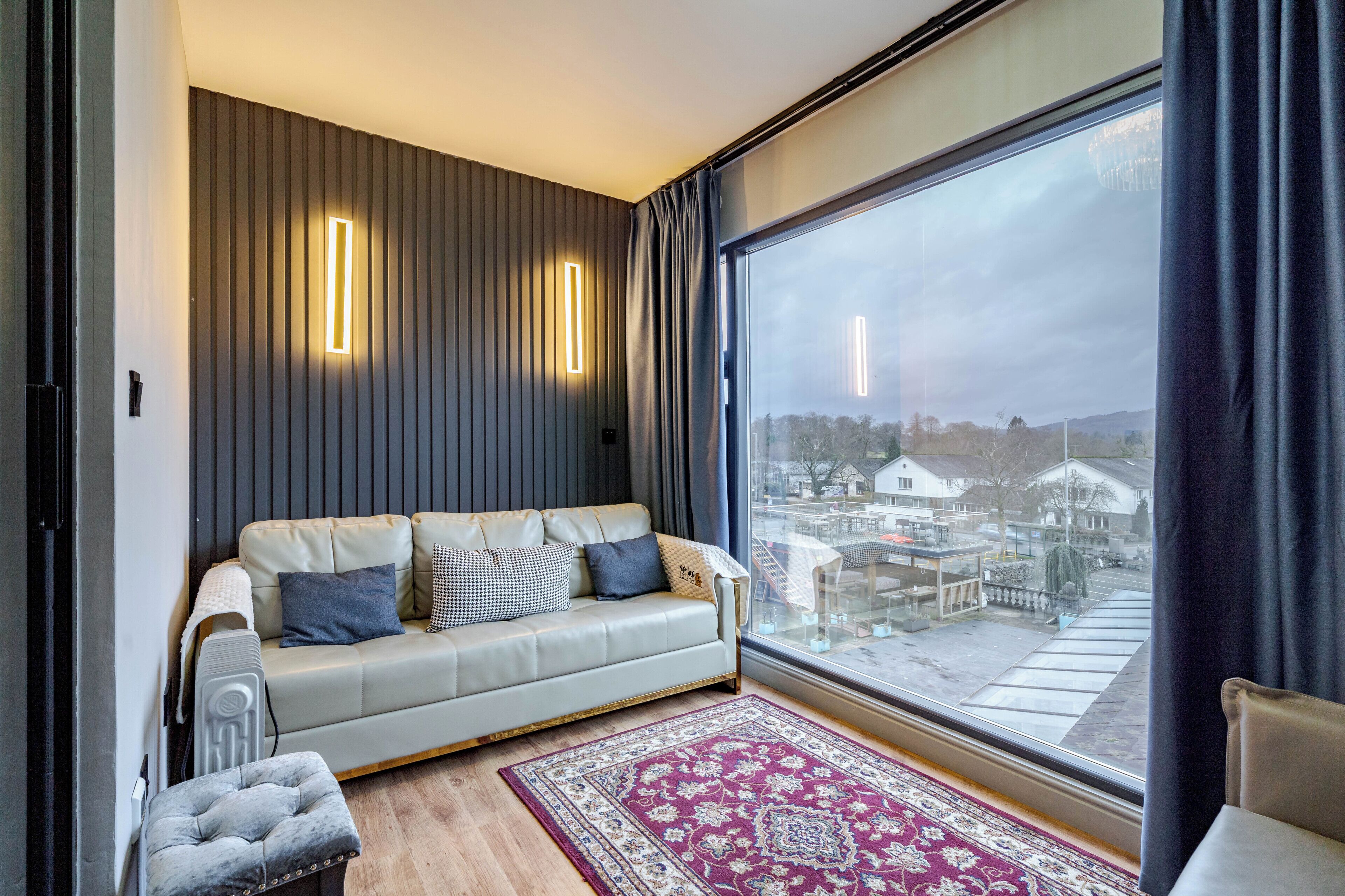 A modern living room with a sofa, a patterned rug, and a large window with curtains.
