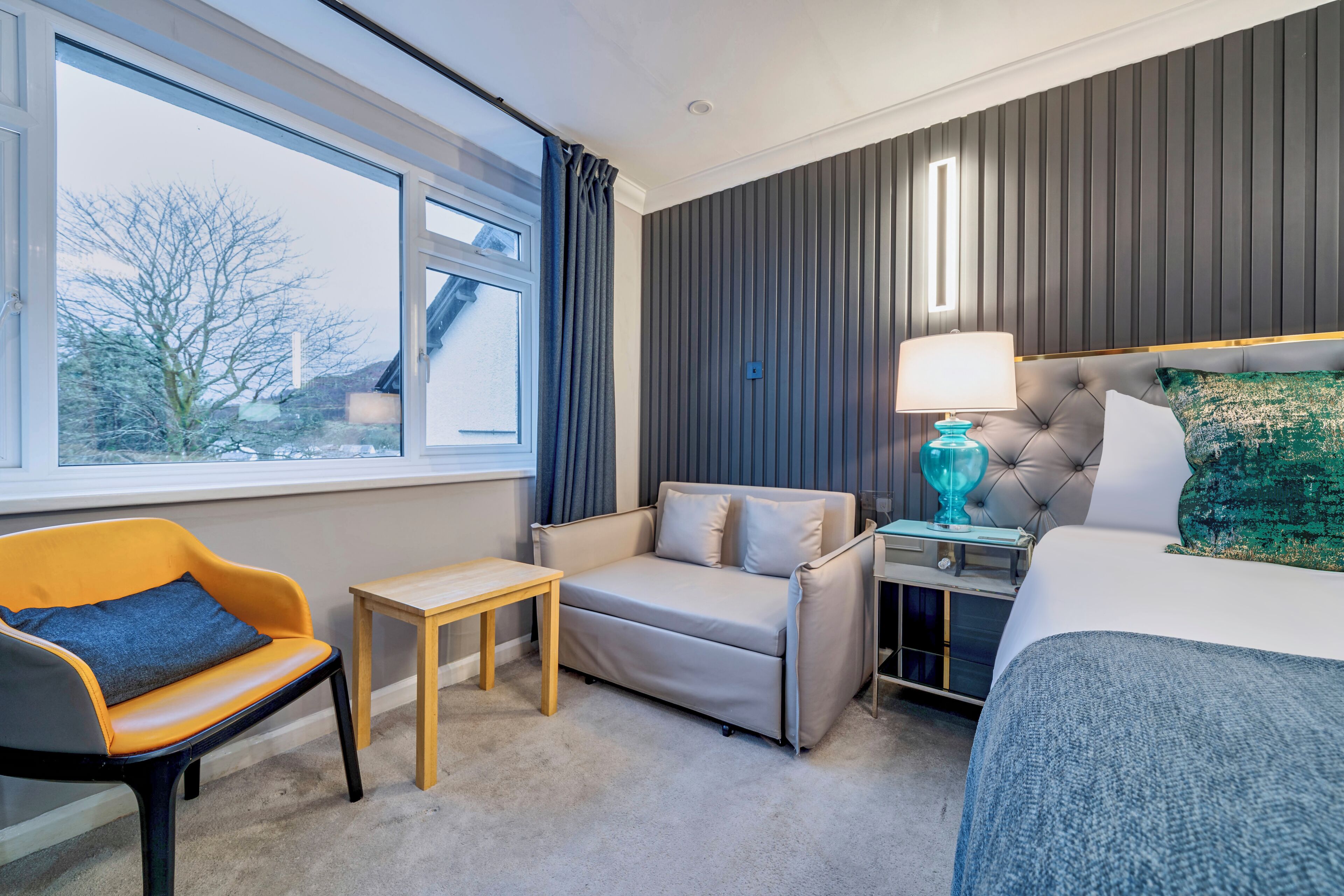 Une chambre d’hôtel avec un canapé, un fauteuil, une petite table, une lampe et un lit.