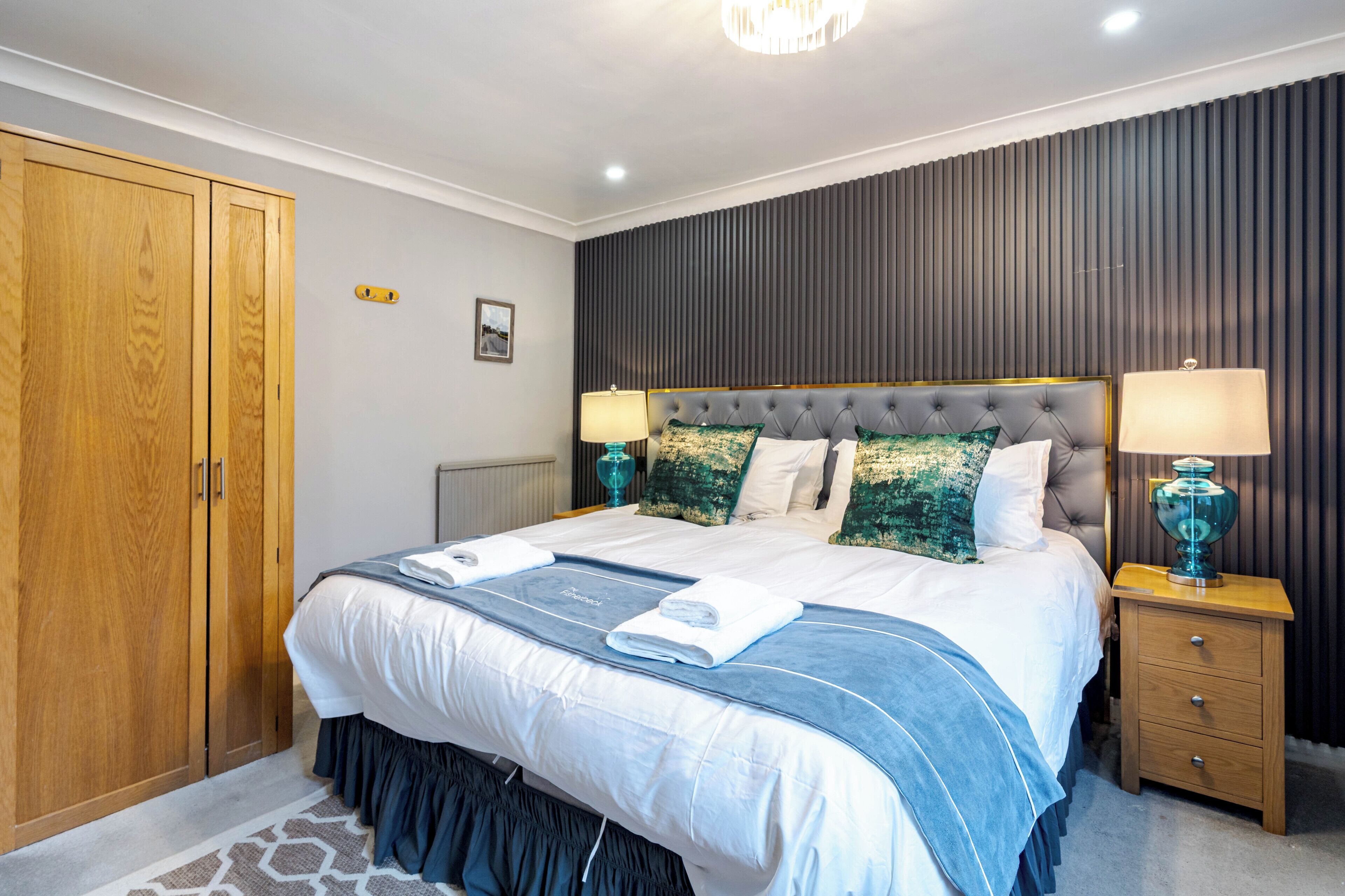 A bedroom with a large bed, wooden wardrobe, and a nightstand with lamps.