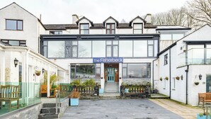 Un edificio con un letrero que dice 'The Fisherbeck' en la entrada, un patio empedrado con piedra y un banco a la derecha.