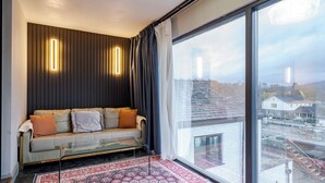 Una habitación moderna con sofá, alfombra estampada, ventana grande y vistas a la ciudad.
