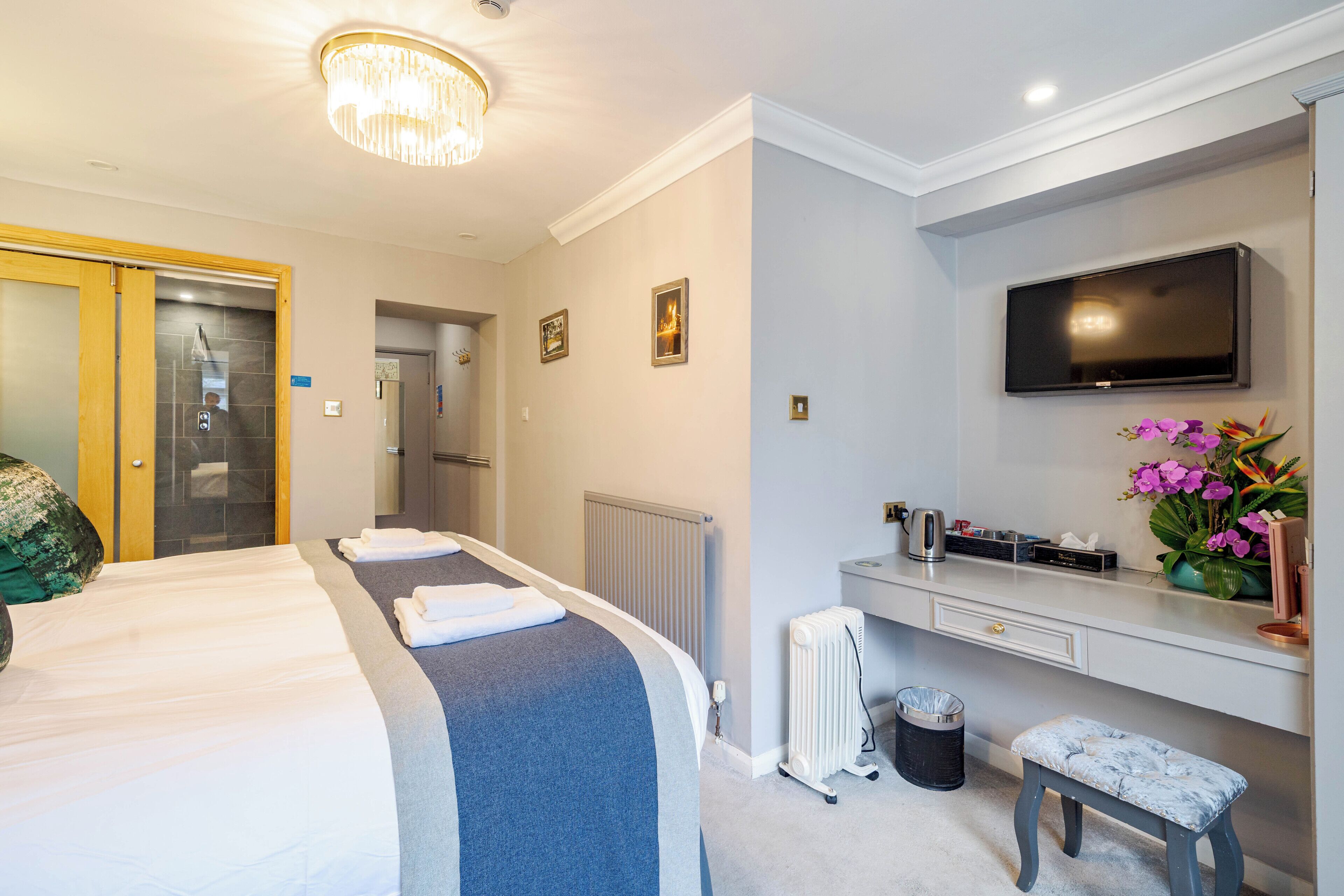 A hotel room with a large bed, a desk with a flat-screen TV, a radiator, and a trash bin.