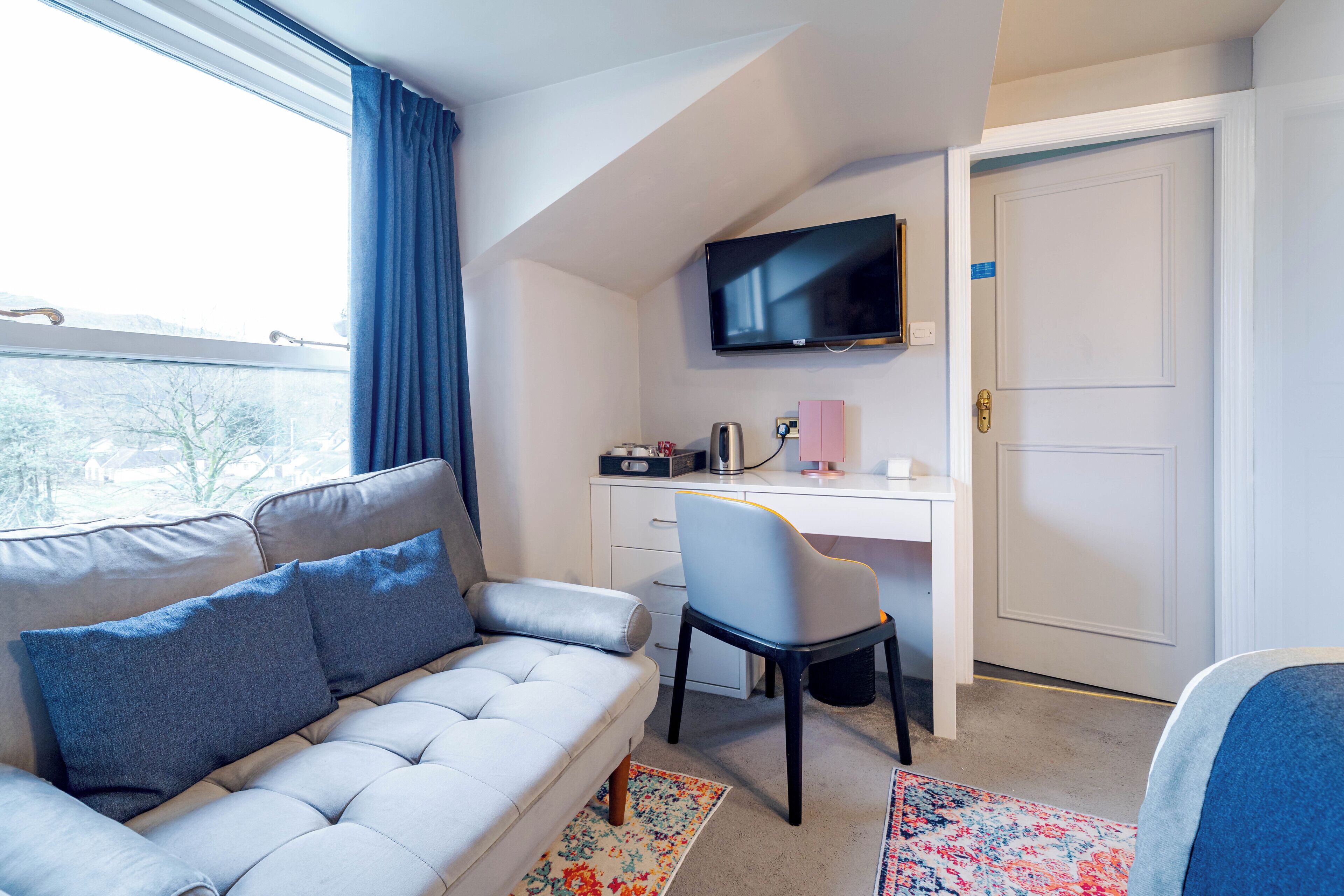 A modern bedroom with a sofa, a desk, a chair, a TV, and a door.