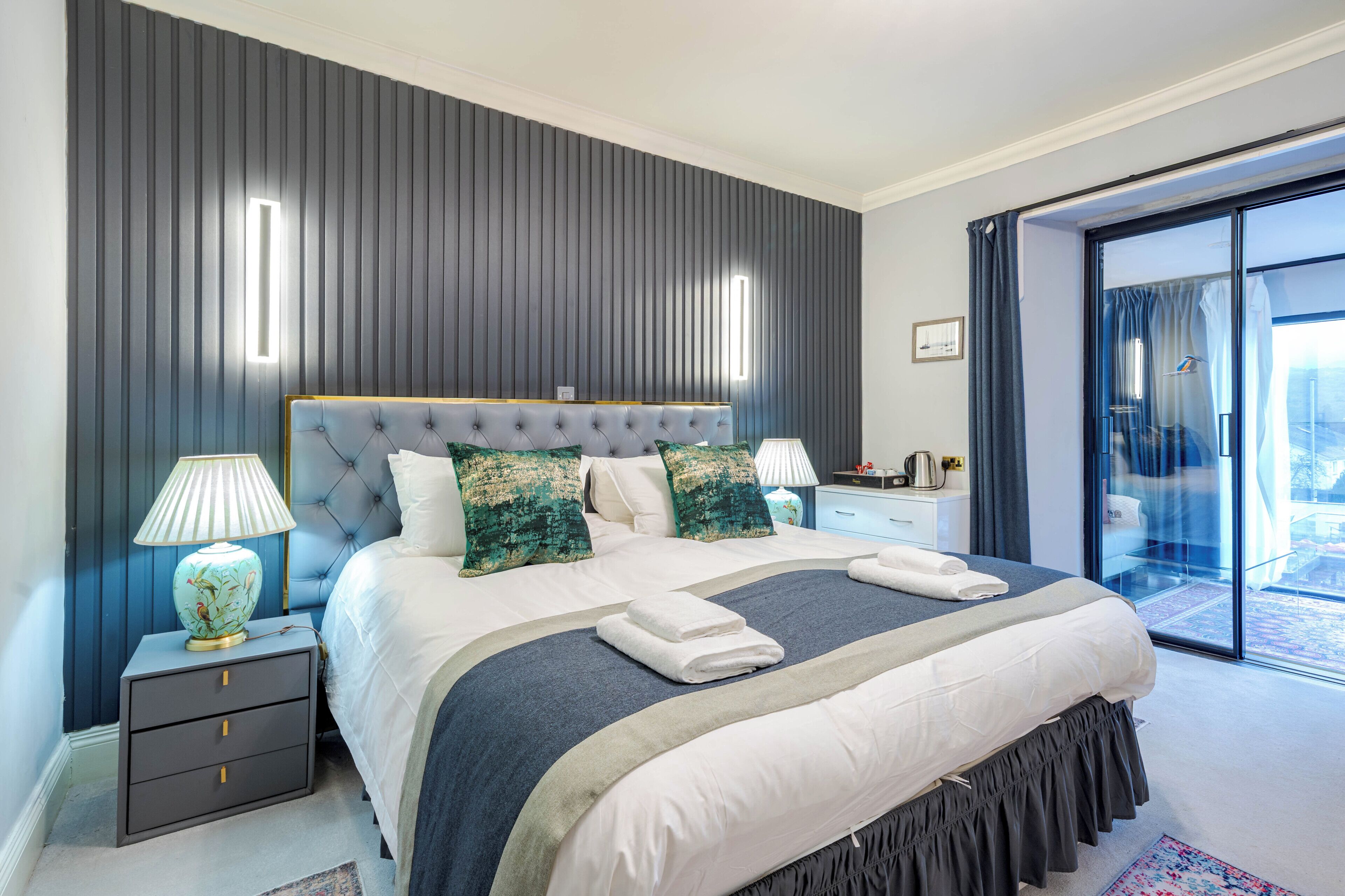 Et moderne hotelværelse med en stor seng, et natbord, en lampe og udsigt til det fri.