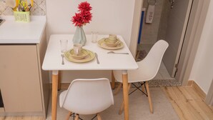 A small dining area with a white table set for two, a vase with red flowers, and a small yellow basket with utensils. - Elite Residence  (Nairobi)