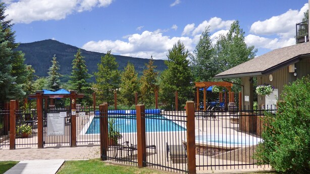 Un jardin avec une piscine, une terrasse en bois et une vue sur les montagnes en arrière-plan.