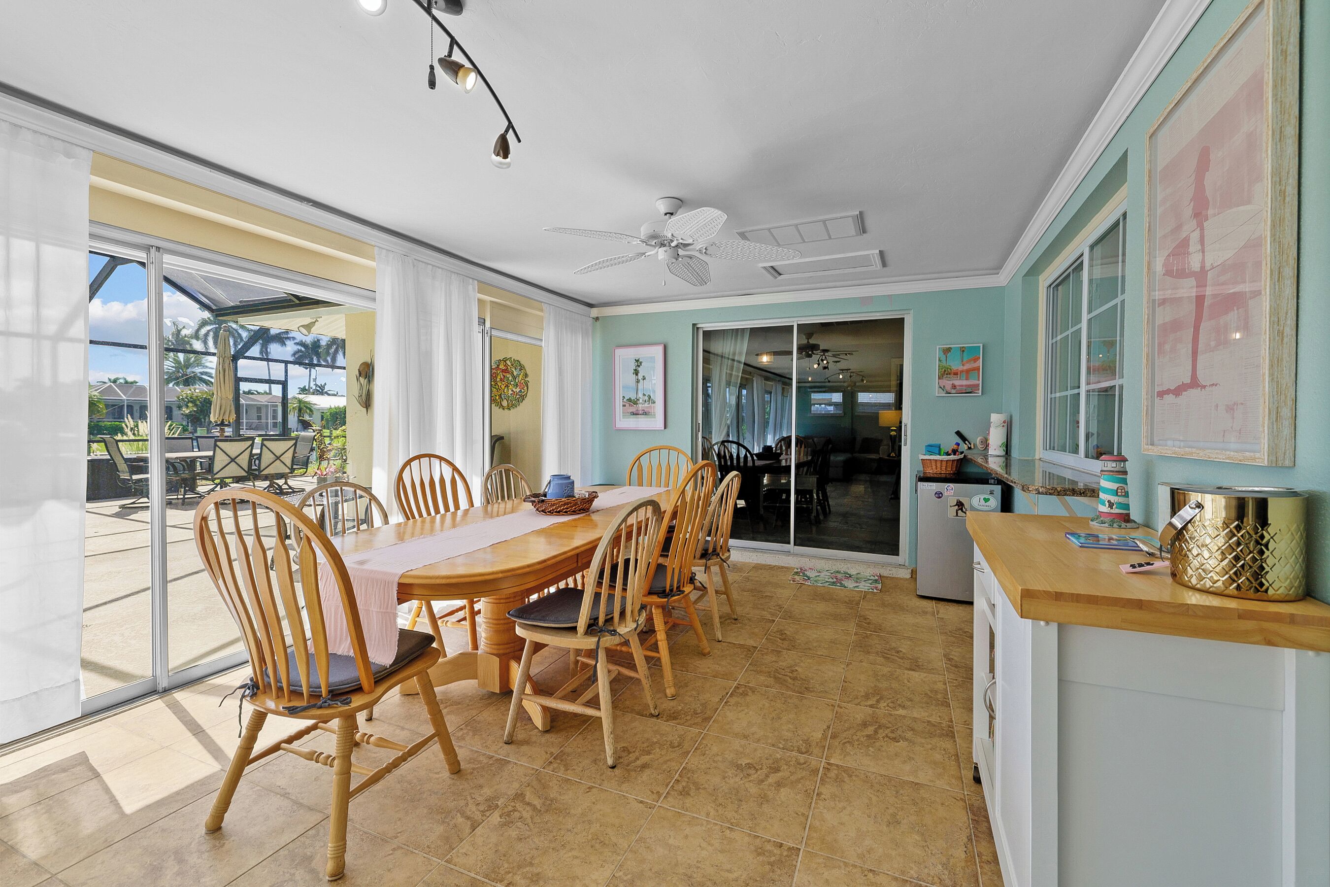 Un espace repas avec une table et des chaises en bois, un ventilateur de plafond et une vue sur une terrasse extérieure, accessible par de grandes portes vitrées.