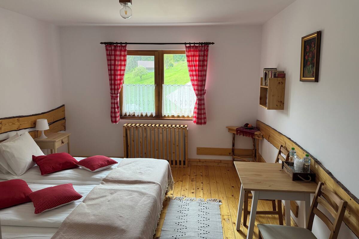 A bedroom with a bed, a wooden nightstand, a table, and a chair.