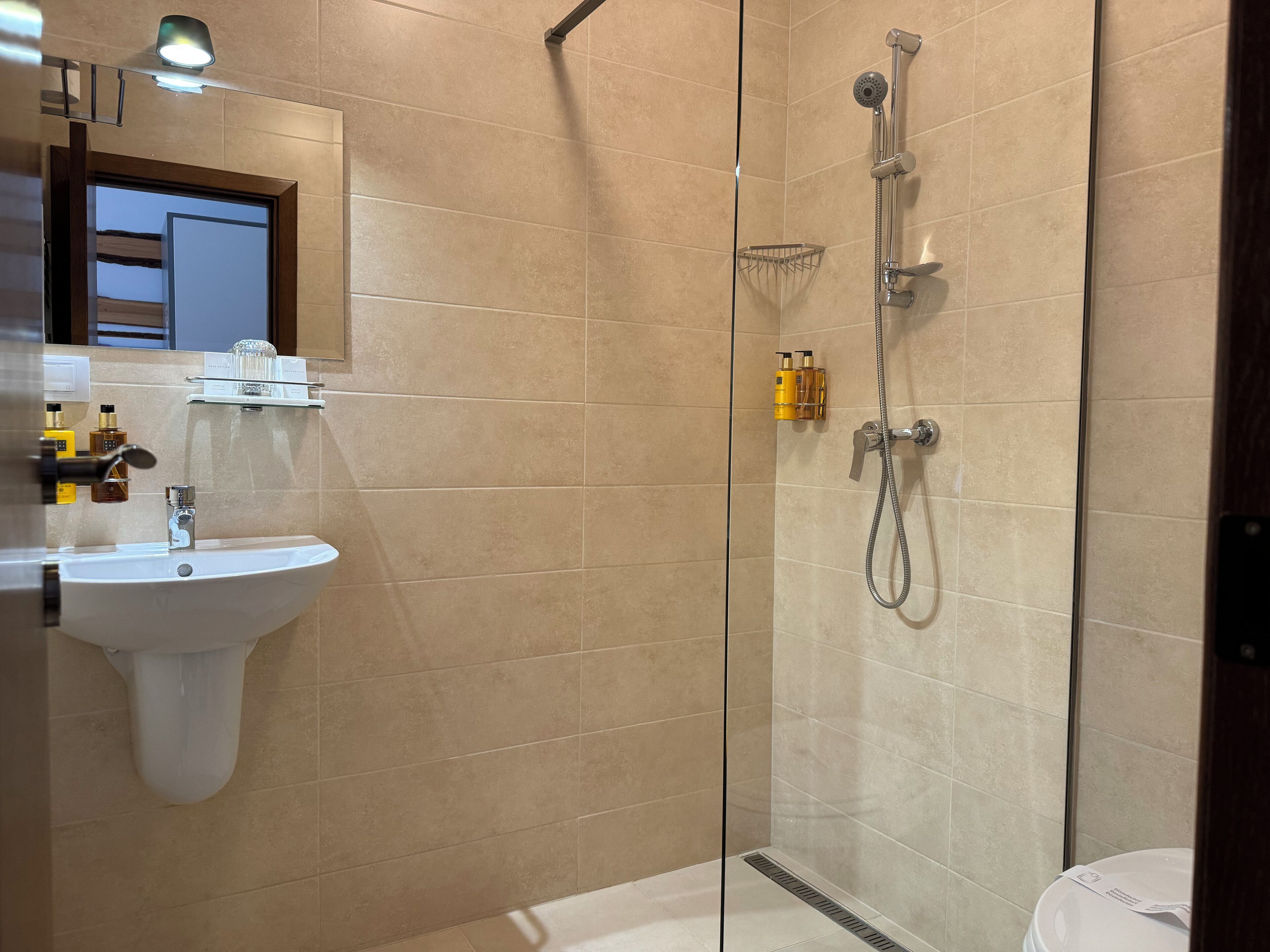 A modern bathroom with a glass-enclosed shower, a sink, and toiletries on the wall.