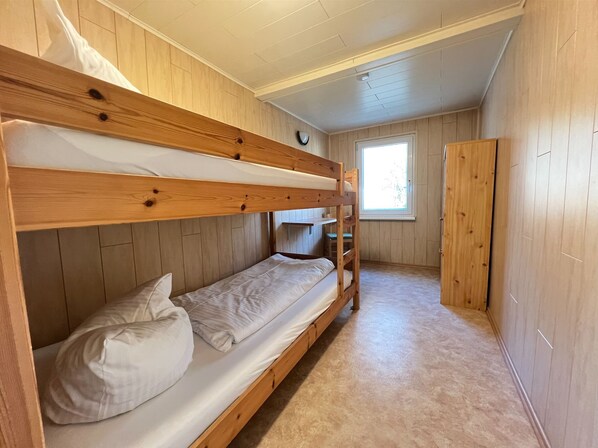 Een slaapkamer met stapelbedden, houten wanden en een raam.