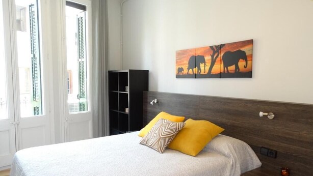 A bedroom with a large bed, a nightstand, a wall-mounted shelf, and a painting of elephants. - Feel at Sants Apartments (Barcelona)