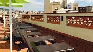 A rooftop terrace with sun loungers and a green umbrella, overlooking a cityscape. - Feel at Sants Apartments (Barcelona)
