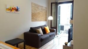 A modern living room with a sofa, a small table, and a lamp. There is a balcony visible through the door. - Feel at Sants Apartments (Barcelona)