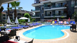 A pool area with lounge chairs and umbrellas, surrounded by a building with balconies. - Nature Maris Apart (Marmaris)