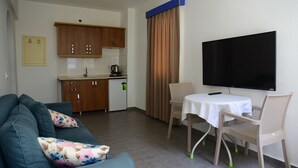 A living room with a sofa, a dining table with chairs, a kitchen area with cabinets and a refrigerator, and a flat-screen TV mounted on the wall. - Nature Maris Apart (Marmaris)