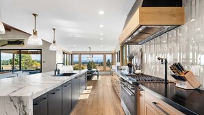 A modern kitchen with a large island, dark cabinetry, and a view of the outdoors.