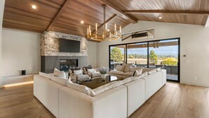 A spacious living room with a large sectional sofa, a fireplace, and a large window offering a view of the outdoors.