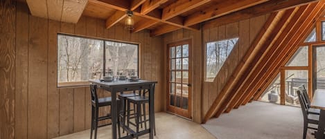 Interior de madera con una mesa de comedor y sillas, ventanas amplias y techo inclinado.