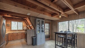 A kitchen with wooden cabinets, a dining table with chairs, and a large window with a view of trees. - Dragonfly Dreams by Innsbrook Vacations! (Innsbrook)