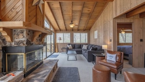 A cozy cabin interior with a stone fireplace, a large sofa, leather armchairs, and a ceiling fan. - Dragonfly Dreams by Innsbrook Vacations! (Innsbrook)