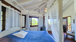 A bedroom with a large bed, a window with curtains, a ceiling fan, and a view of greenery outside. - Casa Maritacas (Sao Sebastiao)