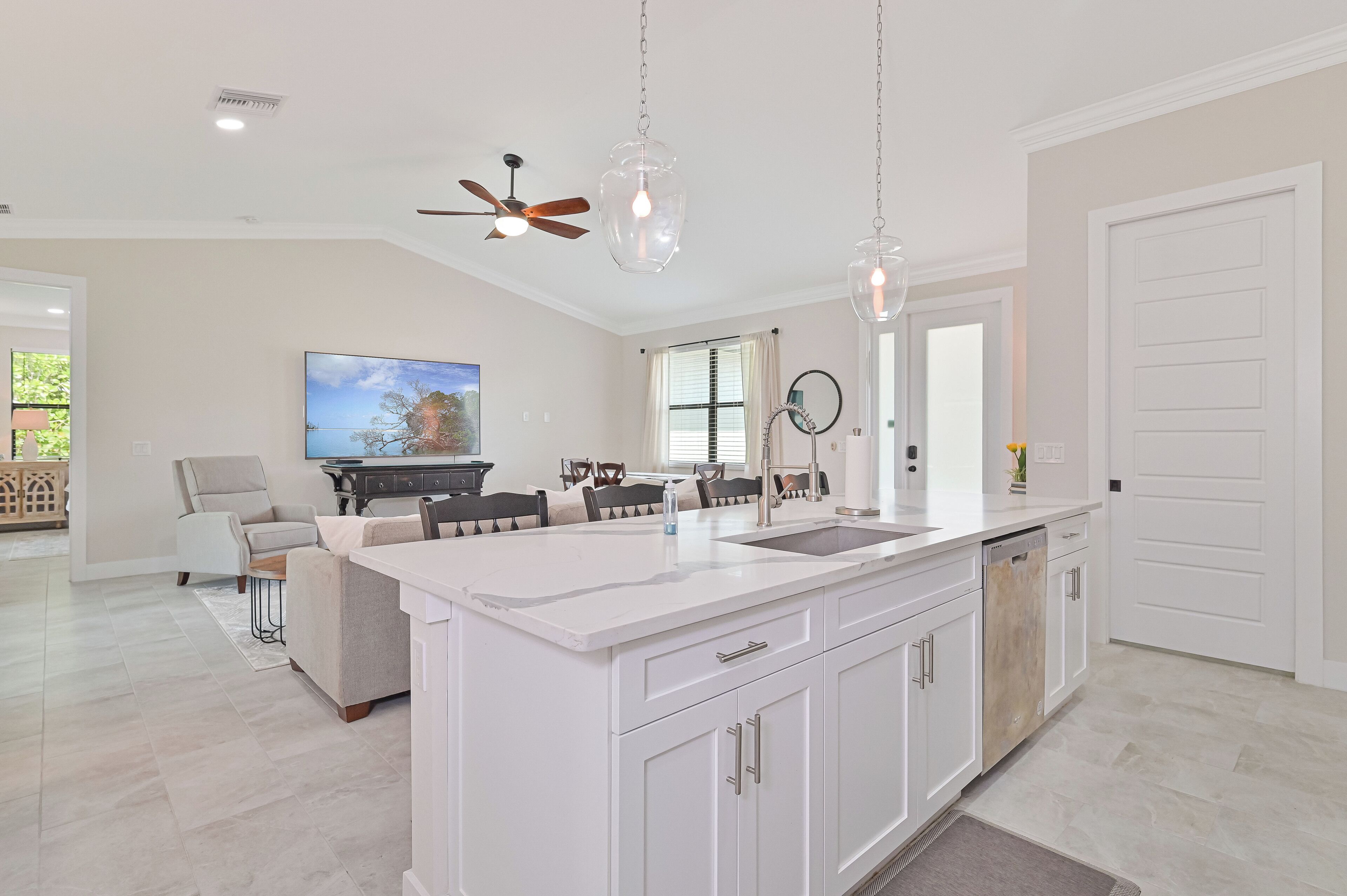 A modern kitchen with white cabinetry, a central island with a sink, and pendant lighting.