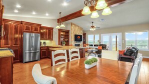 Una cocina amplia con armarios de madera, un refrigerador de acero inoxidable y un comedor con una mesa grande de madera y sillas blancas.