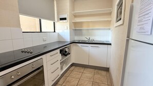 Ett kompakt kök med vita skåp, en svart bänkskiva, en inbyggd ugn och ett kylskåp.