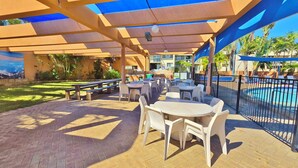 An outdoor patio with tables and chairs, a pool, and a mural. - Riverview Holiday Apartment 50 - Ground Floor -  Kalbarri WA (Kalbarri)