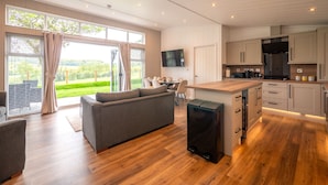 A modern kitchen with wooden cabinets, a built-in island, and a dining area with a grey sofa. - A Stylish Retreat Set in a Scenic Country Club (Blackawton)