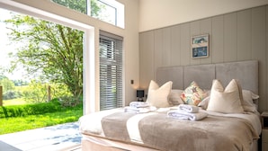 A bedroom with a large bed, a view of greenery outside, and a framed picture on the wall. - A Stylish Retreat Set in a Scenic Country Club (Blackawton)