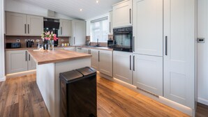 A modern kitchen with white cabinets, a wooden countertop, and a black trash bin. - A Stylish Retreat Set in a Scenic Country Club (Blackawton)