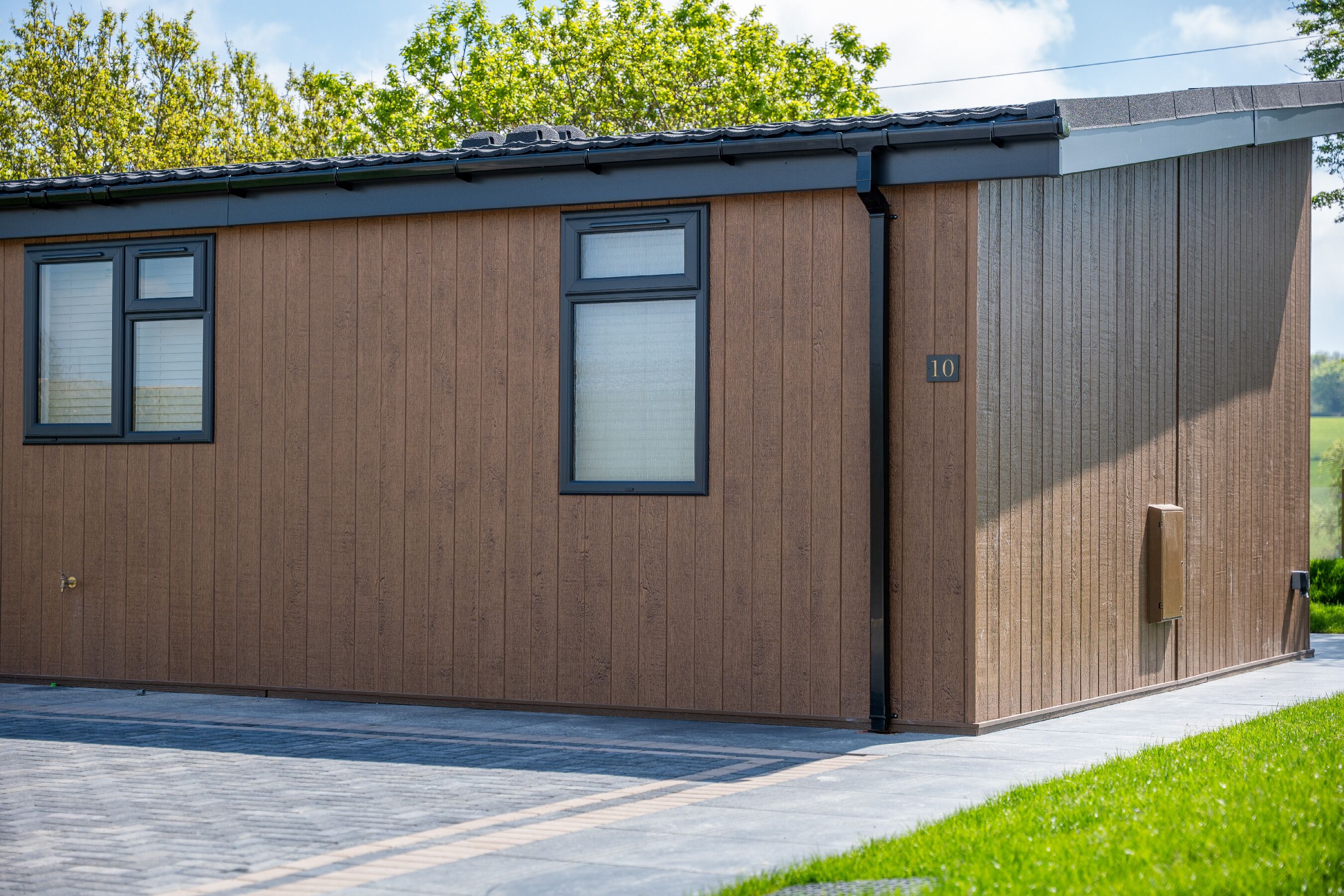Un bâtiment moderne doté de deux fenêtres et d’une porte, d’une enseigne portant le chiffre « 10 », et d’un petit espace extérieur avec un chemin pavé et de l’herbe.