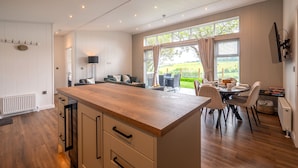 A modern kitchen with a wooden island, white cabinetry, and a dining area with a view of the outdoors. - A Stylish Retreat Set in a Scenic Country Club (Blackawton)