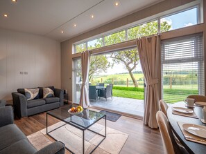 A modern living room with a glass coffee table, grey sofa, and a dining area with a table set for two.