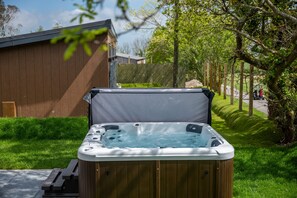 A hot tub in a backyard with a wooden deck and a wooden fence in the background.