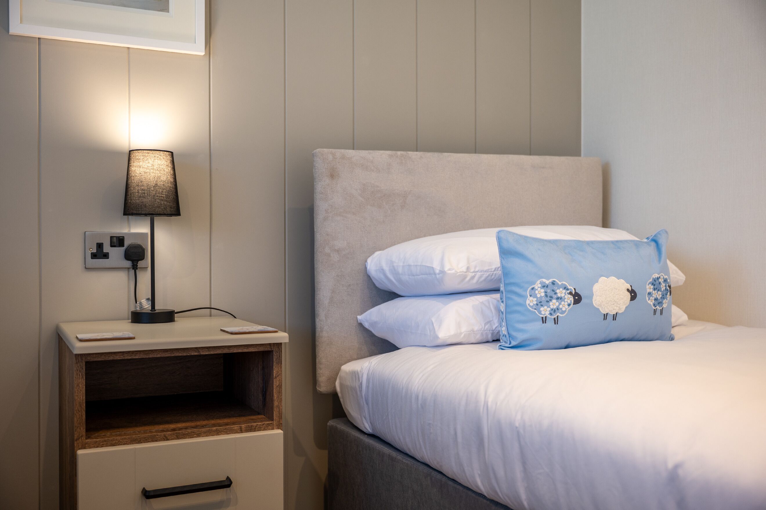 A neatly made bed with white and blue pillows, a bedside lamp, and a wooden nightstand with a drawer.