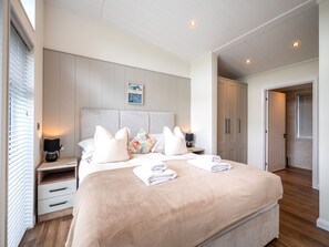 A bedroom with a large bed, bedside tables, a nightstand, a headboard, and a small wall decoration.