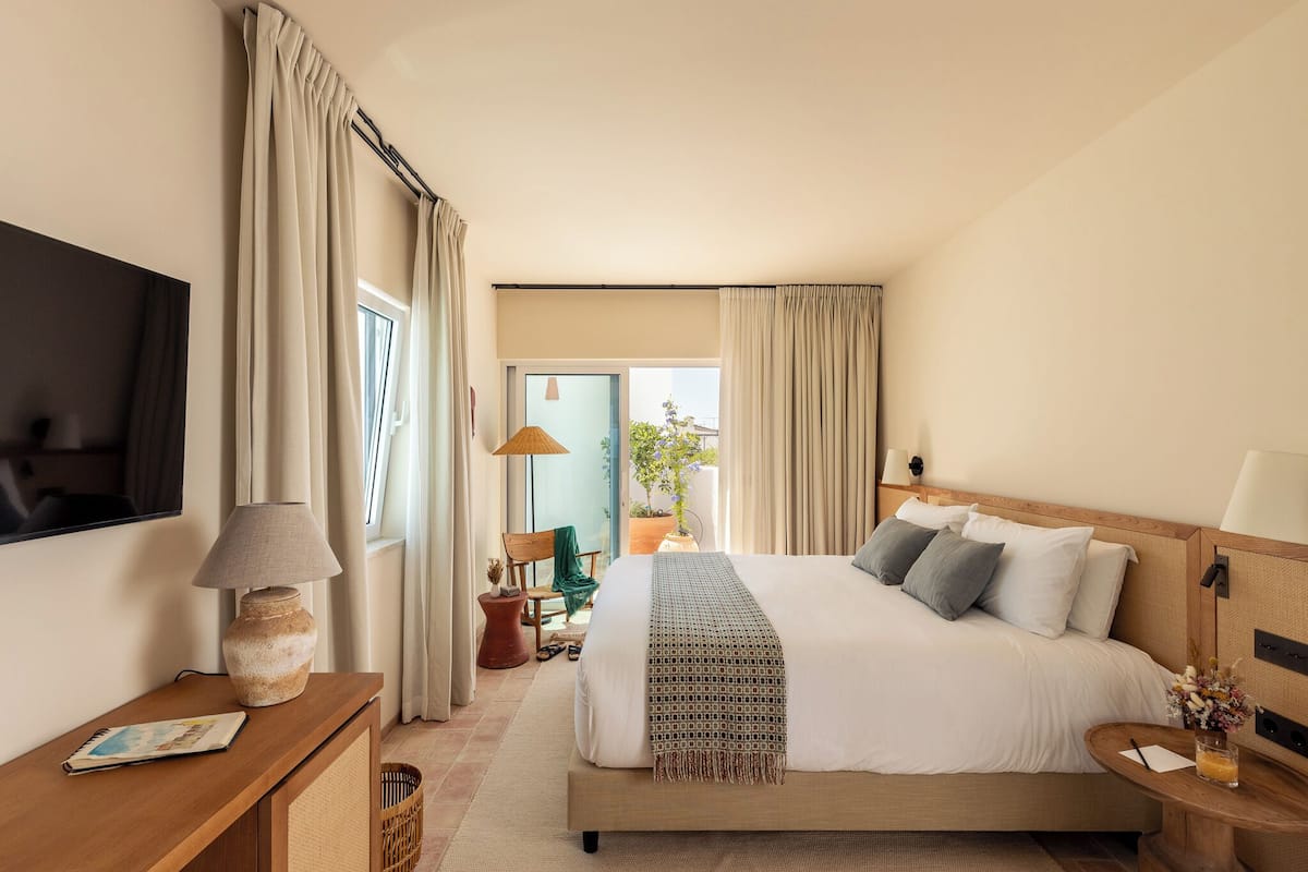 Habitación de hotel con una cama grande, un televisor de pantalla plana, una mesita de noche de madera, una lámpara y vistas al exterior.