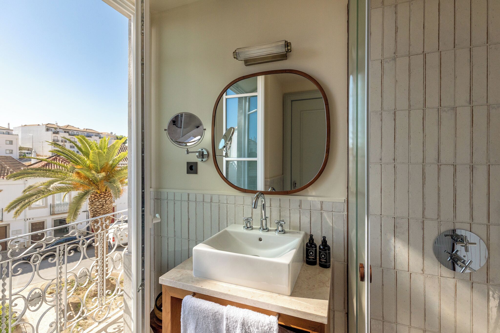 A bathroom with a large sink, a round mirror, and a view of the outside balcony.