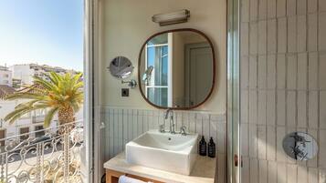 A bathroom with a large sink, a round mirror, and a view of the outside balcony.