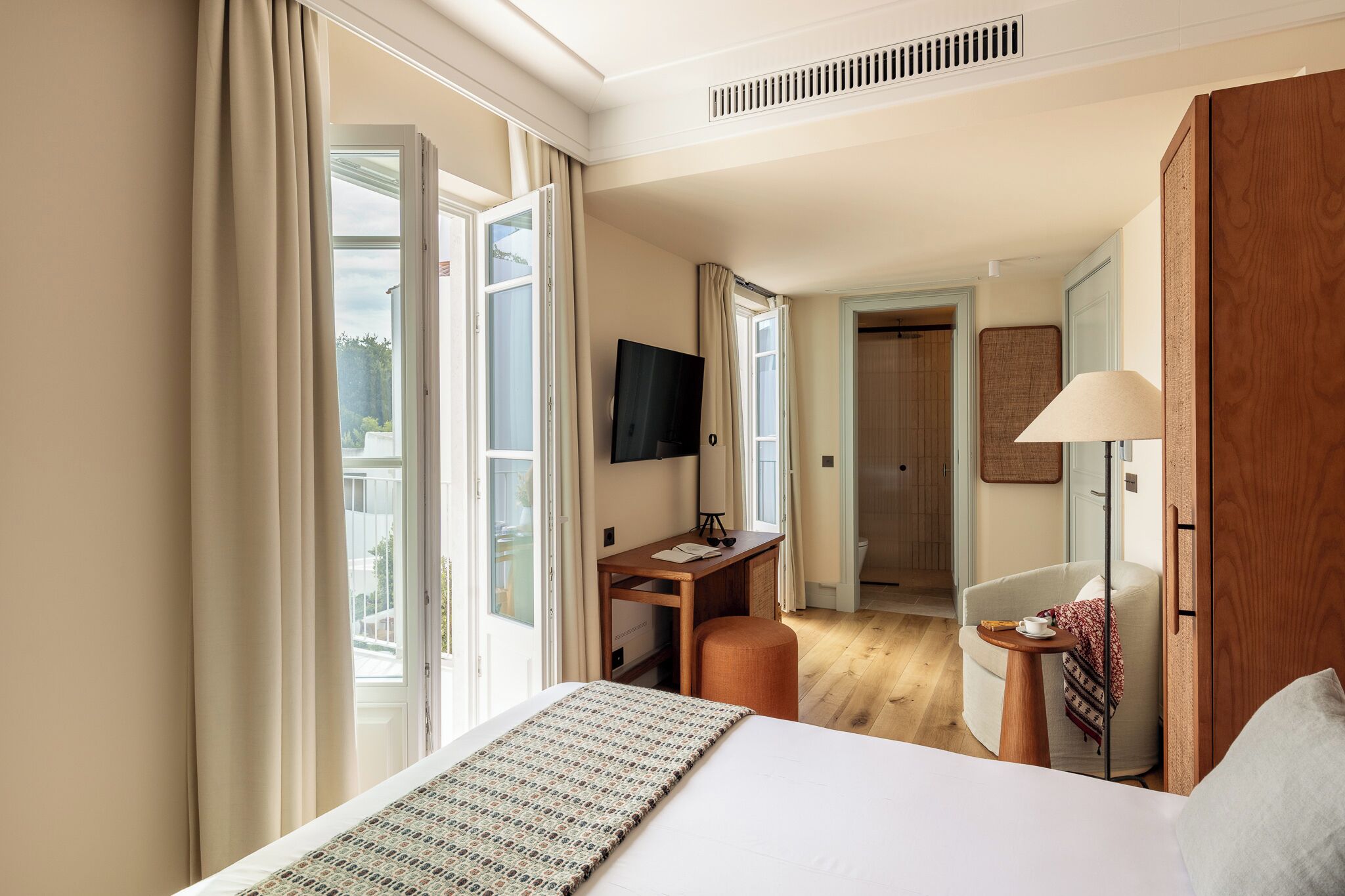 Une chambre d’hôtel avec un lit, un bureau, une chaise, une télévision et une fenêtre avec des rideaux.